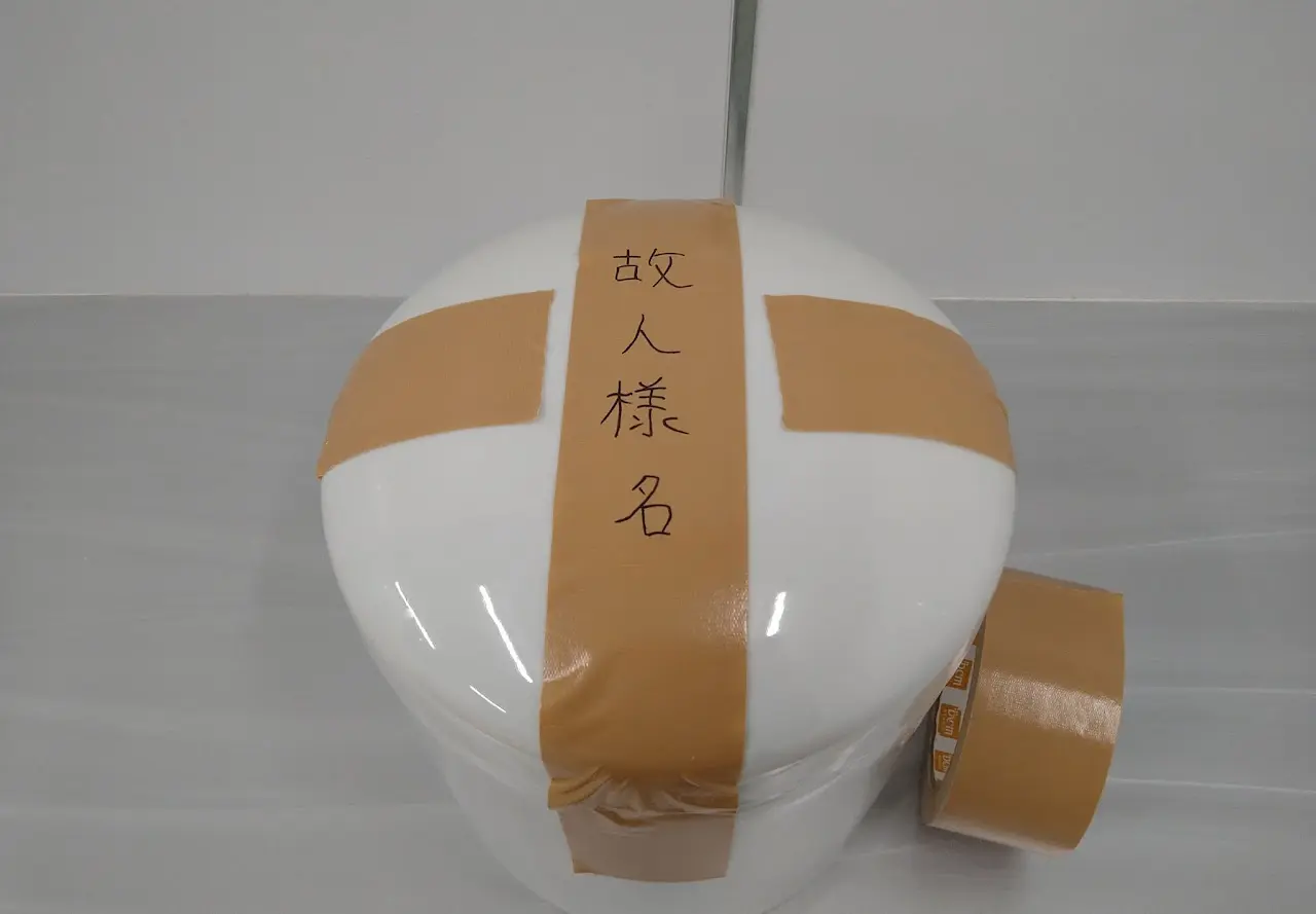 骨壷の蓋をテープで固定し、袋で包む工程（送骨梱包ステップ1）